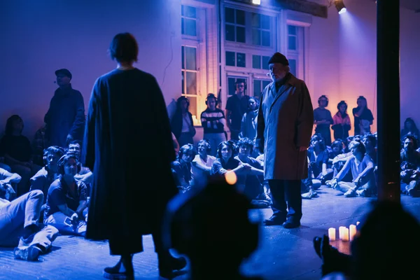 Spectacle immersif "La fin du présent" au Théâtre nouvelle génération à Lyon : deux comédiens, l'un en cape sombre l'autre en trench, devant un public dans une salle tamisée aux lumières bleues et violettes.