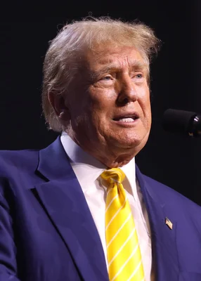 Donald Trump, ancien président des États-Unis, s'adressant à des participants lors d'un rassemblement 'Chase the Vote' à l'église Dream City à Phoenix, Arizona, parlant au microphone en costume bleu foncé, chemise blanche et cravate à rayures jaunes.