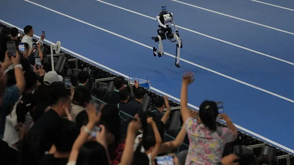 Lors des Jeux de robots à Pékin, un robot humanoïde bipède photographié en plein saut sur la piste bleue de sprint, sous le regard de spectateurs filmant avec leurs smartphones, illustrant la viralité sur TikTok.