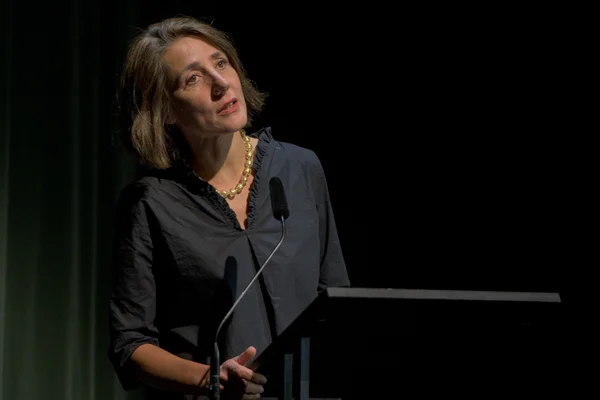 Une femme aux cheveux bruns mi-longs, en chemisier sombre et collier de perles, parlant au podium sur fond sombre lors des 14e Journées littéraires germano-israéliennes à Berlin (septembre 2019) réunissant Dov Alfon et d'autres auteurs.