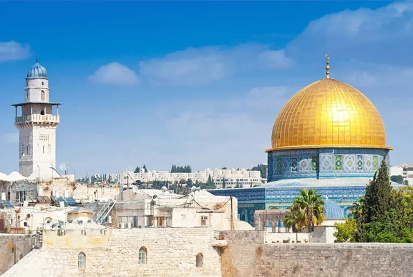 Le Dôme du Rocher avec son dôme doré et ses carreaux bleus, ainsi qu'un minaret, sous un ciel bleu avec des nuages, site incontournable en Israël.