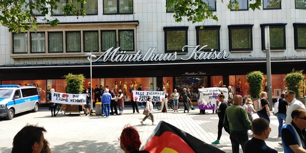 Contre-manifestation devant un stand d'information de l'AfD à Hanovre en 2024, devant le magasin Mäntelhaus Kaiser, avec des personnes tenant des banderoles et un fourgon de police stationné.