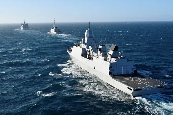 Le gouvernement néerlandais autorise la frégate HNLMS Evertsen (F805, pont hélicoptère) à rejoindre l'escorte du Charles de Gaulle ; ce navire fut localisé par un traceur Bluetooth caché dans une carte postale, vu ici en mer avec deux autres navires.