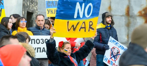 Dans le cadre de la réunion d'urgence de l'Assemblée générale sur l'Ukraine où le chef de l'ONU appelle à l'arrêt des combats, photographie de manifestants dont une femme tenant une pancarte 'NO WAR' aux couleurs du drapeau ukrainien.
