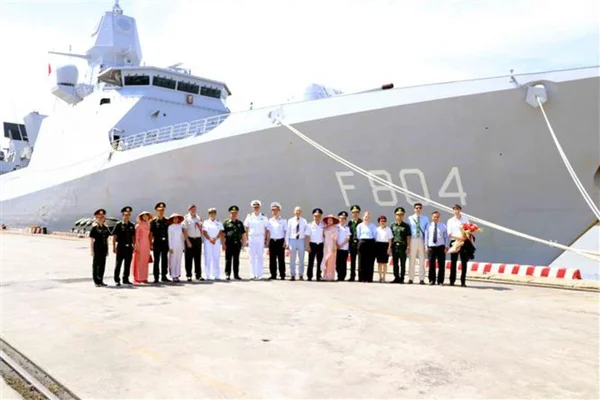 Un navire de la Marine royale néerlandaise à quai à Hai Phong, identifiable par le numéro F804, avec un groupe de militaires et de civils posant pour une photo sur le dock devant le bâtiment gris.