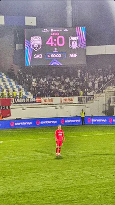 Photographie de nuit du match Sabah contre Aarhus du 11 août 2026, montrant un joueur en maillot rouge sur le terrain et un tableau d'affichage indiquant 4-0 entre SAB et AGF.