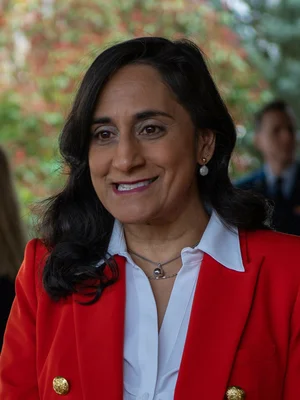 Anita Anand, ministre canadienne de la Défense, femme aux cheveux foncés vêtue d'une veste rouge et d'une chemise blanche, souriant légèrement en extérieur, s'entretenant avec des représentants de presse à Ramstein, Allemagne, le 21 avril 2023, sur le soutien canadien à l'OTAN pour l'Ukraine.