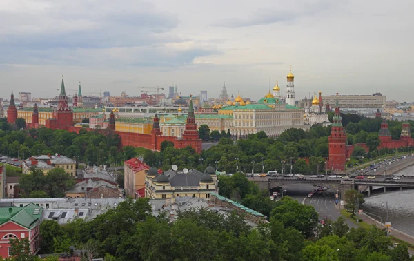 Vue grand angle du Kremlin de Moscou montrant murs de brique rouge, tours à flèches vertes et dorées, cathédrales à dômes dorés, la Moskva et un pont avec circulation.