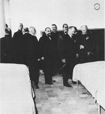 Photographie historique en noir et blanc de 1933 : Albin Peyron, le président Albert Lebrun et l'architecte Le Corbusier en costumes sombres, debout entre deux lits lors de l'inauguration de la Cité de Refuge à Paris.