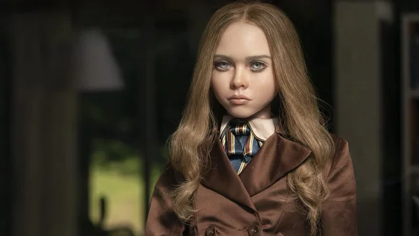 Portrait en gros plan de la jeune actrice Violet McGraw en costume, portant un manteau brun avec une chemise à col et une cravate rayée, dans la bande-annonce officielle du film M3GAN.