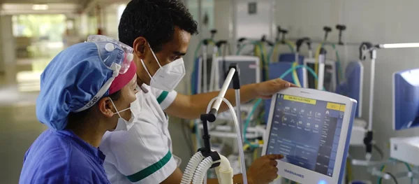 Deux professionnels de santé portant masques et équipements de protection observant l'écran d'un ventilateur dans un hôpital, dans le cadre de la préparation à la prochaine pandémie.