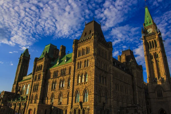 La colline du Parlement à Ottawa, en Ontario, Canada, montrant le Centre Block avec la tour de la Paix et son architecture néo-gothique sous un ciel bleu parsemé de nuages.