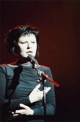 Guesch Patti chantant en concert lors du Printemps de Bourges en 1991, coiffée de cheveux courts foncés et vêtue d'un haut sombre à manches longues.