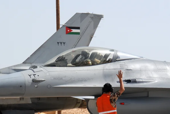 Vue de la base aérienne d'Azraq : un chasseur F-16 de la force aérienne jordanienne au sol avec un pilote dans le cockpit et un membre du personnel en gilet orange signalant à proximité.