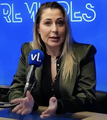 La productrice télé Magali Berdah prise de parole devant un fond bleu, avec une barre bleue portant le logo 'VL' visible, portant un blazer vert foncé