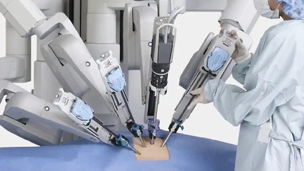 Un professionnel médical en blouse et bonnet chirurgical ajustant les bras robotiques du système chirurgical da Vinci sur un patient simulé.