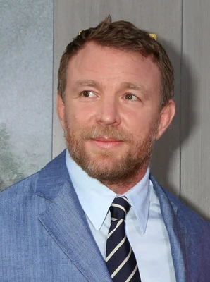 Portrait en gros plan de l'acteur Simon Pegg en costume bleu chemise claire et cravate rayée, regardant légèrement à sa droite.