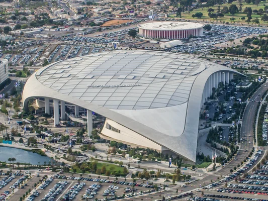 Vue aérienne du stade SoFi à Inglewood, Los Angeles, avec son toit translucide caractéristique et l'arène Kia Forum en arrière-plan.