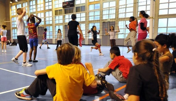 Un groupe d'enfants joue au volley-ball dans un gymnase. Des enfants sont en action sur le terrain tandis que d'autres observent depuis les gradins, illustrant le type d'activité scolaire concernée par la fuite de données.