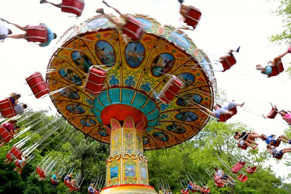 Balançoire colorée en mouvement dans le parc d'attractions Dollywood de Dolly Parton, avec des cavaliers suspendus dans des chaises rouges, sur fond d'arbres verts et de ciel bleu éclairé.