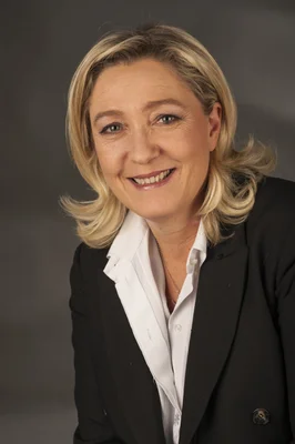 Portrait professionnel de Marine Le Pen, souriante, avec des cheveux blonds, portant un blazer noir par-dessus une chemise blanche à col.