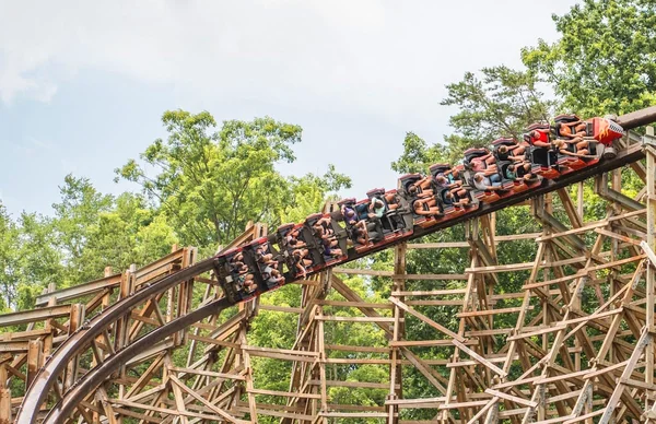 Montagnes russes en bois remplies de passagers montant une pente raide dans le parc Dollywood de Dolly Parton, entourées de végétation luxuriante sous un ciel partiellement nuageux.