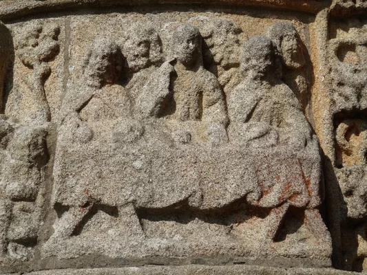 Détail d'un bas-relief en pierre usée représentant des figures assises autour d'une table, intitulé "la chaire à prêcher" à Pleubian.
