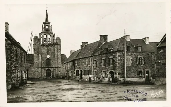 Photographie d'archives en noir et blanc de la place principale de Pleubian avec son église à tour carrée et les bâtiments environnants, montrant le centre historique du village breton.