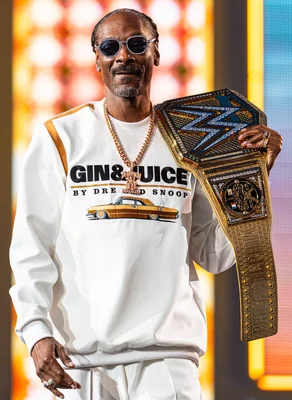 Snoop Dogg portant des lunettes de soleil et une chemise blanche 'Gin & Juice', tenant une ceinture de championnat lors du WrestleMania XL en avril 2024.