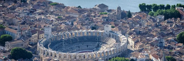 Vue aérienne de l'Amphithéâtre romain d'Arles, imposant monument antique ovale entouré des toits en terre cuite de la ville, avec le fleuve Rhône visible en arrière-plan