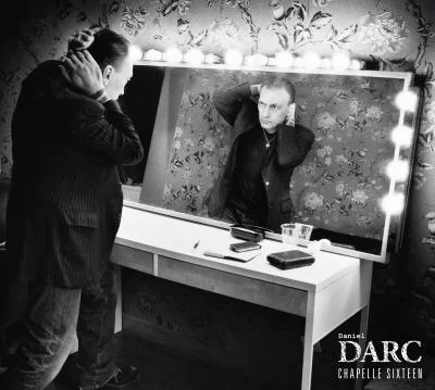 Pochette de l'album "Chapelle sixteen" de Daniel Darc, photographie en noir et blanc du chanteur ajustant ses cheveux devant un miroir de loge entouré d'ampoules