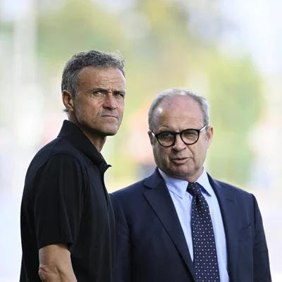 Luis Enrique en polo noir à gauche et Luis Campos en costume sombre avec lunettes à droite, posant côte à côte en extérieur, respectivement entraîneur et conseiller sportif du PSG