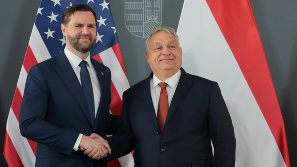 JD Vance en costume sombre serrant la main de Viktor Orban devant les drapeaux américain et autrichien lors d'une visite officielle en Hongrie
