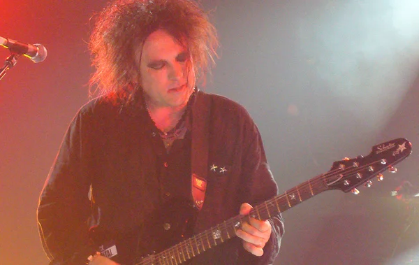 Robert Smith de The Cure jouant de la guitare électrique sur une scène illuminée par des lumières rouges et blanches lors du festival Rock en Seine.