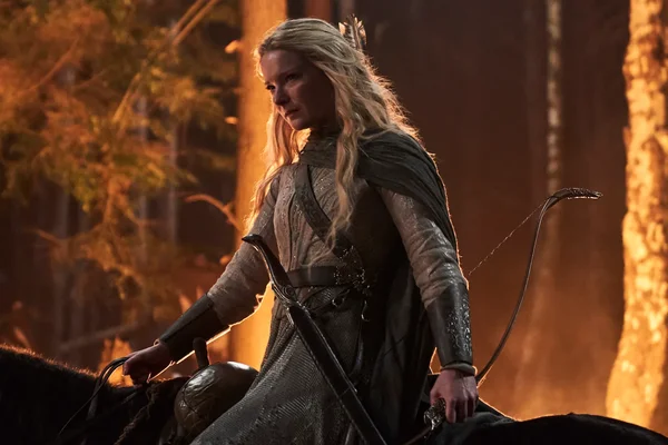 Femme blonde en armure médiévale et cape verte assise à cheval en forêt, tenant un arc et regardant sur le côté, scène issue de la bande-annonce de la saison 2 de The Rings of Power