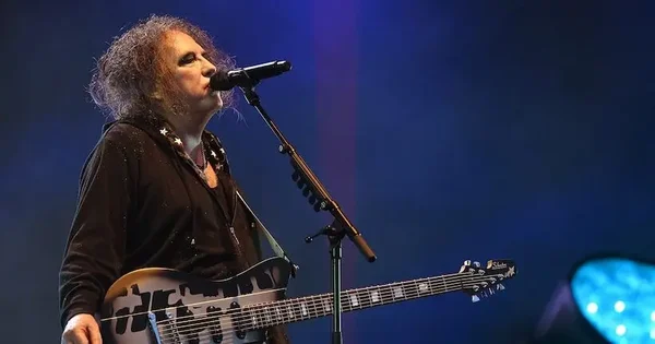 Robert Smith chantant et jouant de sa guitare noire et blanche signature sous des éclairages bleus lors d'un concert, une guitare identique à celle mise aux enchères pour MSF.