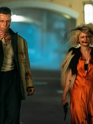 Christian Bale et Jessie Buckley dans The Bride, marchant dans une rue de nuit, cheveux en désordre, maquillage ensanglanté; Jessie Buckley en robe orange avec un pistolet, Christian Bale en veste avec des chiffres sur le front.