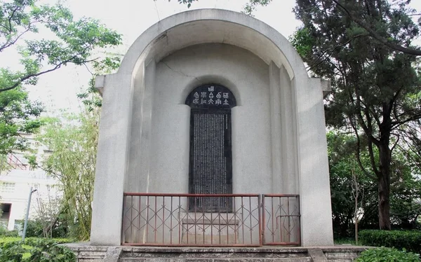 Monument de l'Université nationale associée du Sud-Ouest (Lianda) à Kunming, stèle en pierre à sommet arrondi avec plaque sombre, entourée d'arbres et d'une barrière métallique.