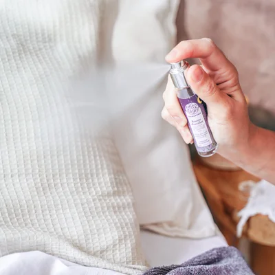 Main humaine pulvérisant la brume Terracurma Brume Boréale à base d'huile essentielle de lavandin biologique sur un oreiller blanc texturé - Terraroma