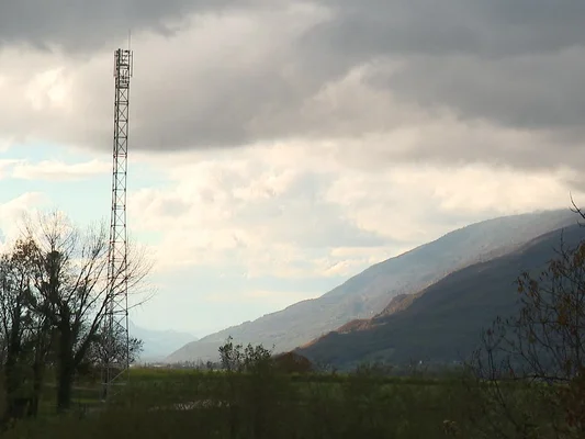 Antenne relais en acier dans un champ herbeux avec des arbres dépouillés, sous un ciel nuageux, en Haute-Savoie.