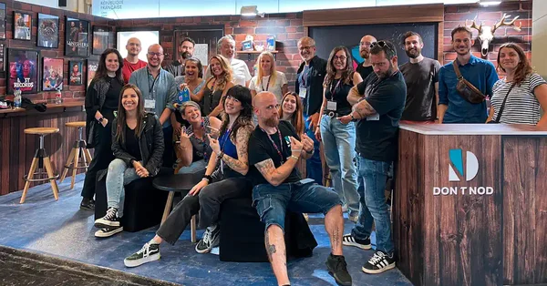 Photo de groupe de collaborateurs du studio Don't Nod posant devant le logo de l'entreprise et des posters de jeux vidéo lors d'un salon professionnel.