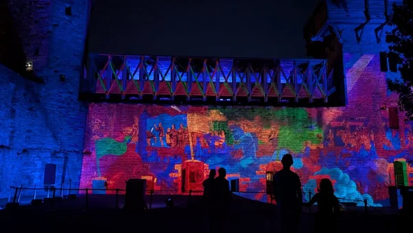 Spectacle de projection lumineuse sur un grand rempart en pierre de Carcassonne lors de 'Remparts et Lumières 2025', avec des silhouettes de spectateurs en premier plan.