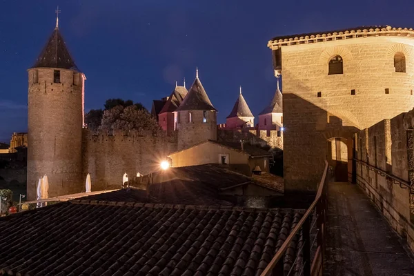 Vue nocturne de la Cité médiévale de Carcassonne illuminée lors de l'événement 'Remparts et Lumières', montrant tours en pierre, créneaux et toits au ciel bleu sombre.