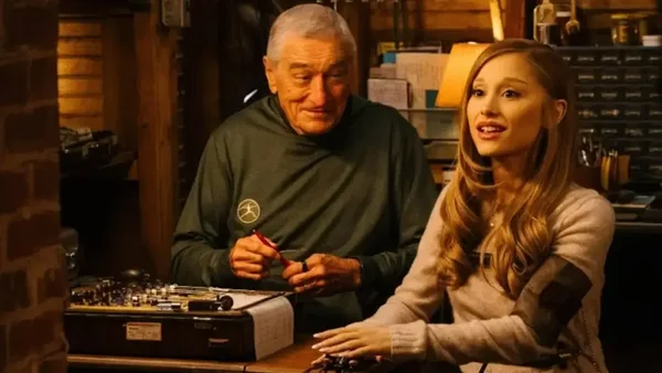 Scène de la bande-annonce de 'Focker In-Law' où Ariana Grande, en pulls beige, passe un test de détecteur de mensonges avec Robert De Niro, en chemise verte.