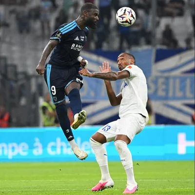 Lassine Sinayoko du Paris FC, en maillot bleu, saute pour une tête lors du match contre l'OM au Vélodrome, où il a inscrit un triplé historique.