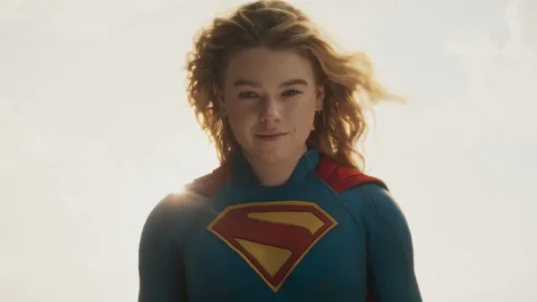 Milly Alcock en costume de Supergirl avec une cape rouge et le bouclier 'S' sur la poitrine, sur fond de ciel bleu.