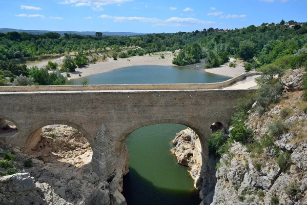 Vue en plongée du pont du Diable, un ancien pont-aqueduc romain enjambant une rivière dans une gorge rocheuse avec une végétation luxuriante.