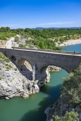 Le pont du Diable, pont en pierre enjambant une rivière aux eaux turquoise, entouré de falaises rocheuses et d'arbres verdoyants, avec des promeneurs traversant.