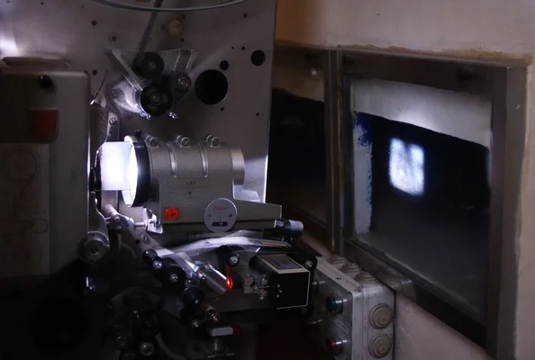 Projecteur cinématographique 35 mm en fonctionnement dans une cabine de projection, avec le faisceau lumineux visible traversant une vitre vers l'écran.