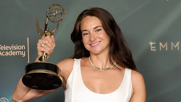 Une femme aux cheveux longs et à la robe blanche, tenant un trophée Emmy avec fierté, lors des Creative Arts Emmys 2026.